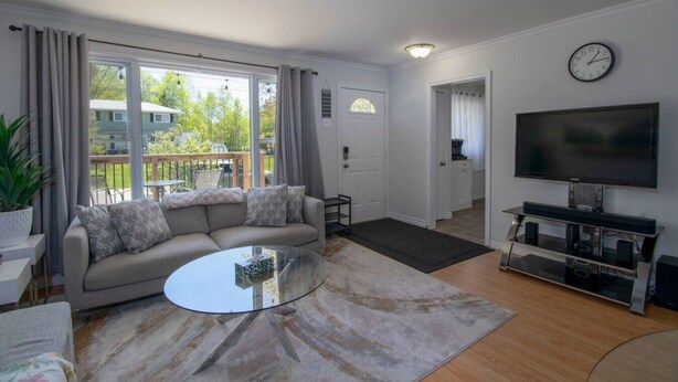 A living room with a sofa, a coffee table, a TV, and a large window. - 3 Bdrm | BBQ | Fire Pit - Steps to Waterfront Park (Port McNicoll)