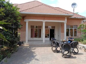 A house with a tiled roof, a covered porch with chairs, and a satellite dish.