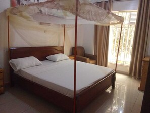 A bed with a canopy, a chair, and a window with curtains.