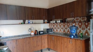 A kitchen with wooden cabinets, a countertop, a water dispenser, and a microwave. - Sunset Retreat Home (Kigali city)