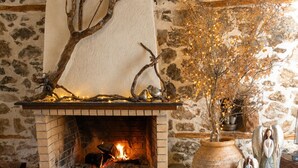 Una chimenea con un fondo de pared de piedra, una mesa de madera rústica con vasos, y un jarrón con ramas secas.
