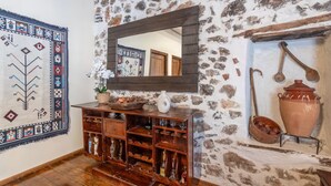 Un interior rústico con pared de piedra, estanterías de madera, un espejo y cerámica tradicional.