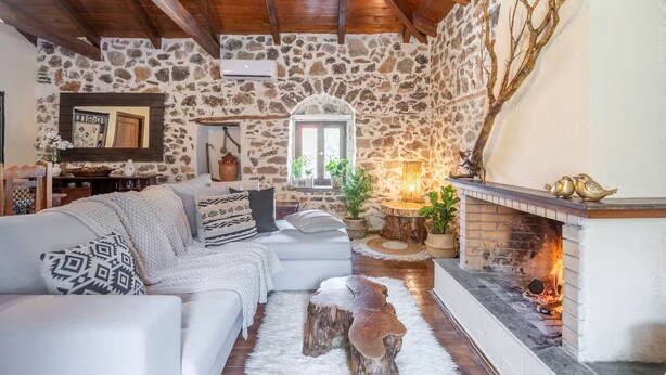Una sala de estar acogedora con una pared de piedra, una chimenea, un sofá y techo de madera.