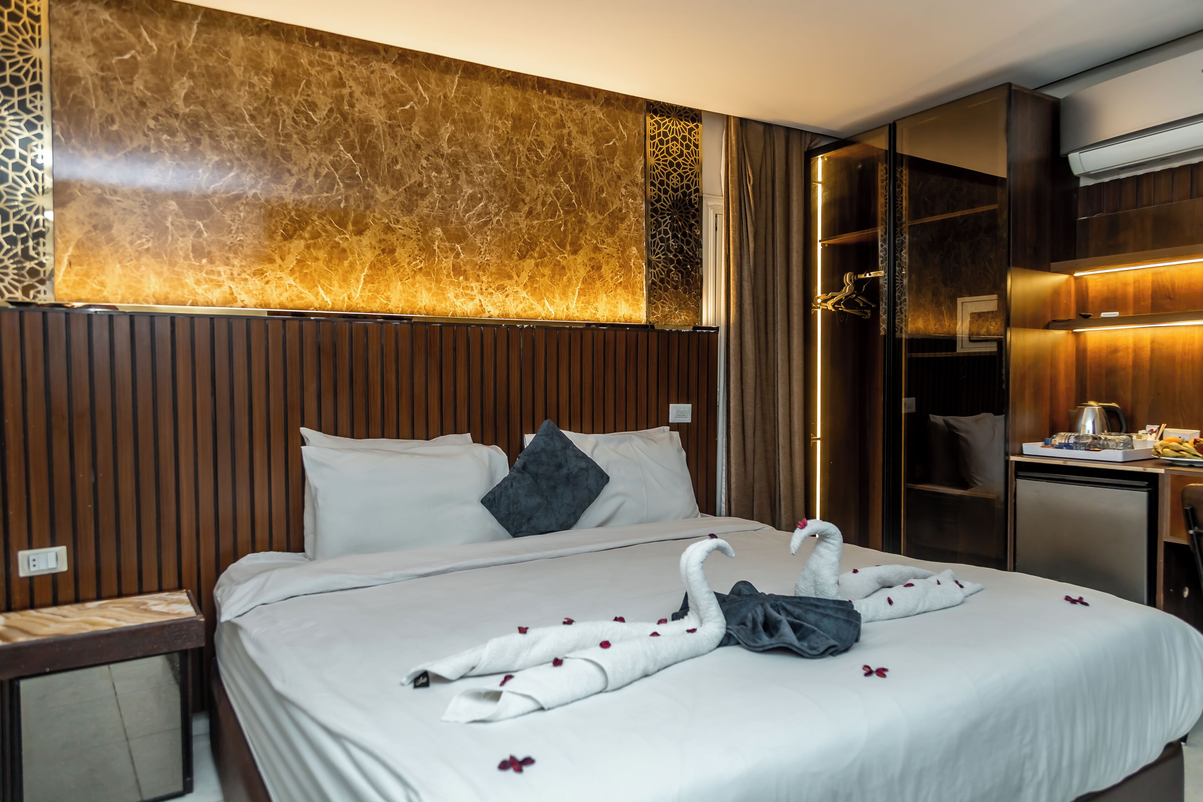 A hotel room with a bed, a wooden headboard, a minibar, and a desk with a lamp.