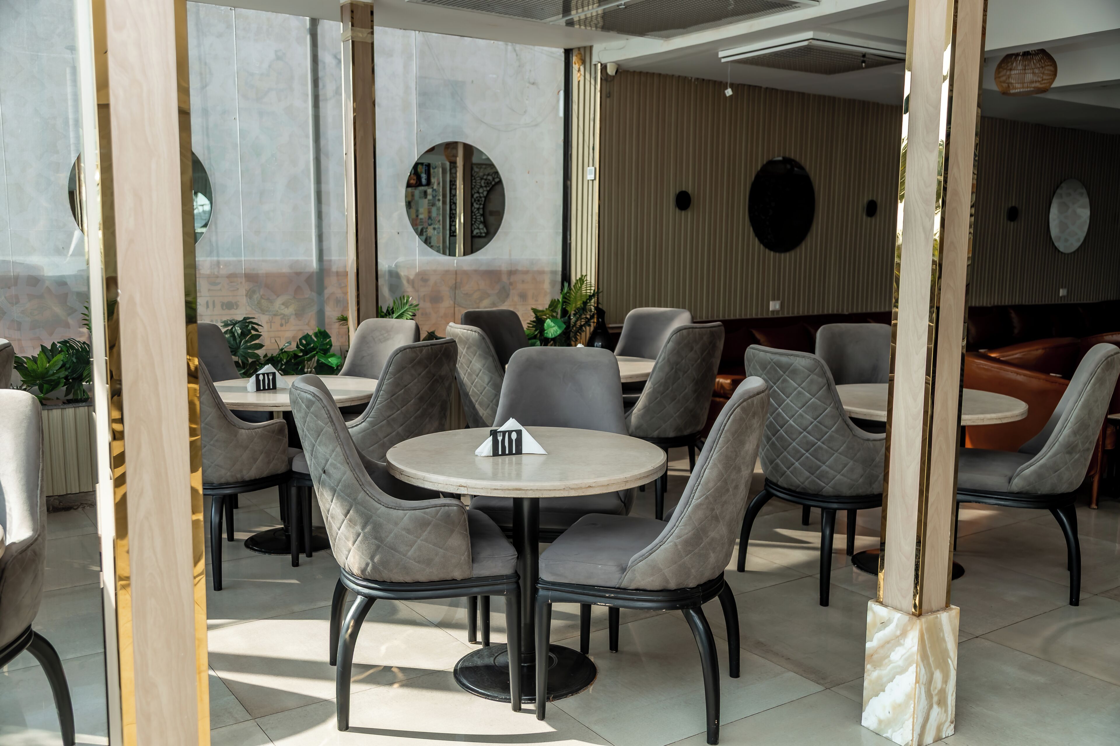 A restaurant with round tables and cushioned chairs, a wooden column, and a tiled floor.