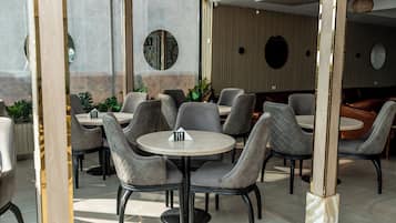 A restaurant with round tables and cushioned chairs, a wooden column, and a tiled floor.
