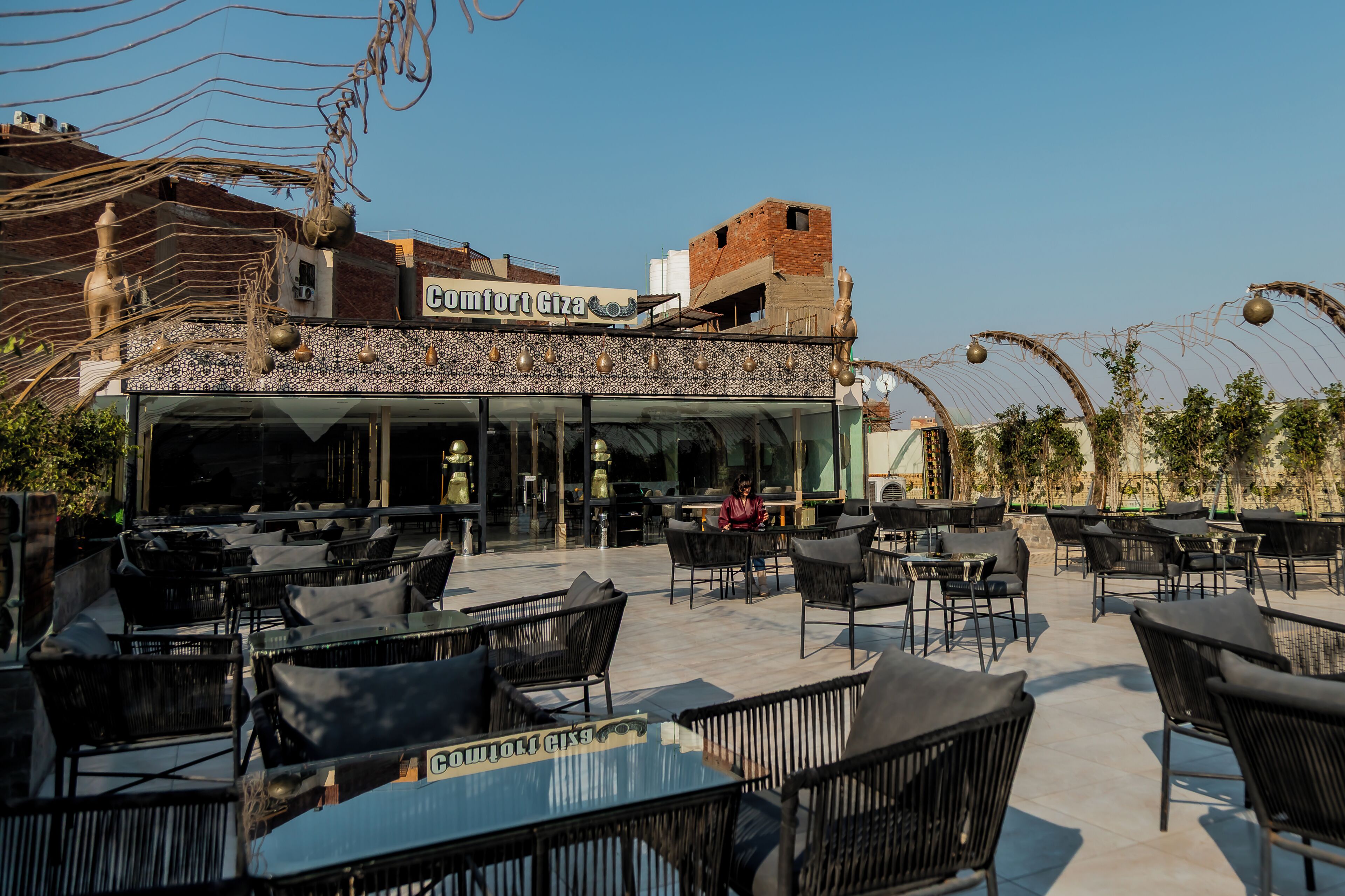 Un café al aire libre con mesas y sillas, un edificio con un letrero y cielo despejado.