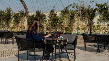 A person seated at a table with a laptop, surrounded by outdoor chairs and tables.