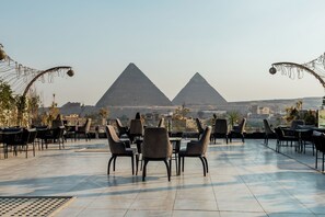 Un espace extérieur aménagé avec des tables et des chaises, une vue sur les pyramides et un ciel dégagé.