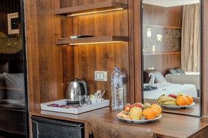 Un miroir à cadre en bois reflétant un lit, une table de chevet avec une bouilloire, une bouteille d’eau et des fruits.