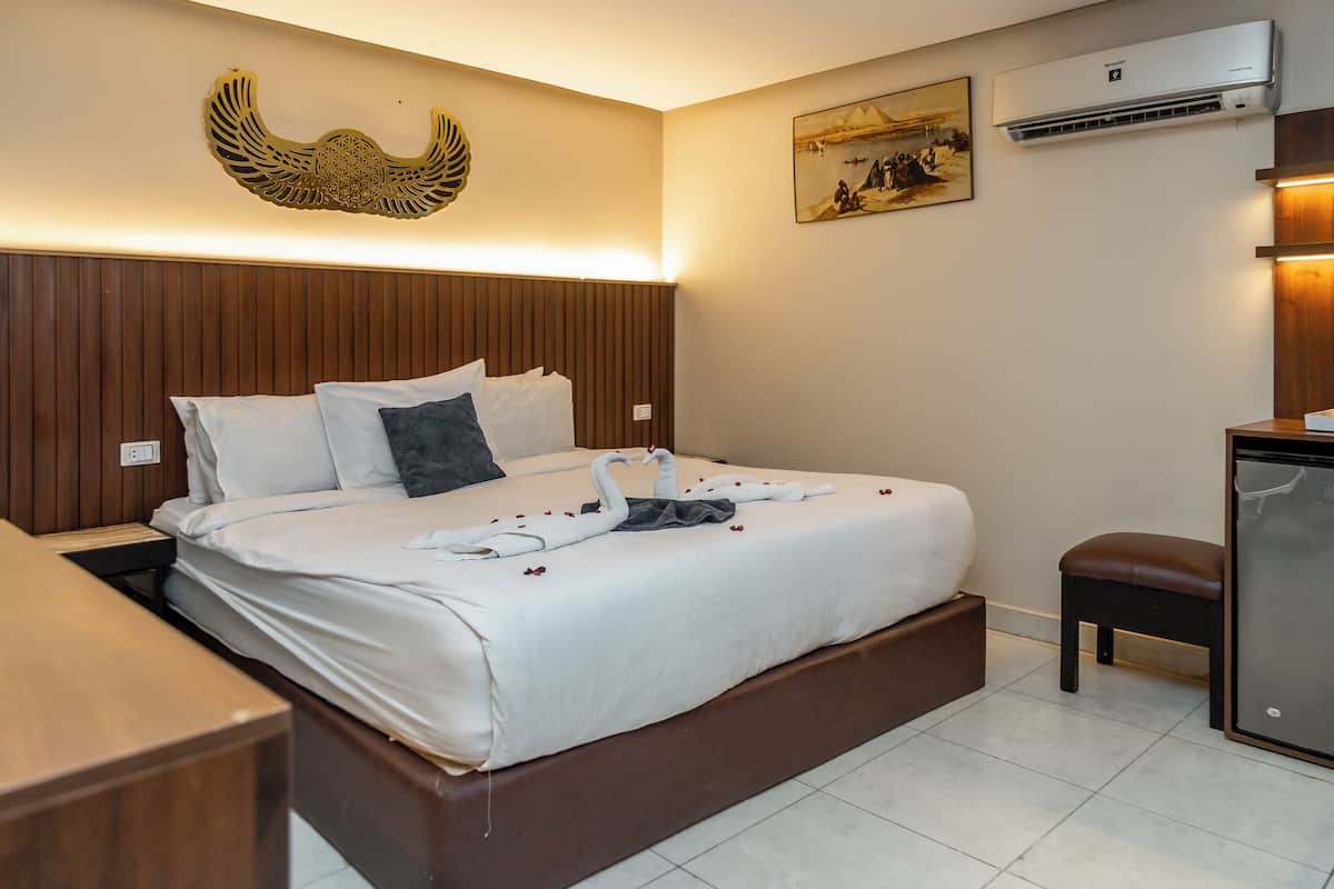 Habitación de hotel con cama, escritorio, silla, aire acondicionado y una obra de arte en la pared.