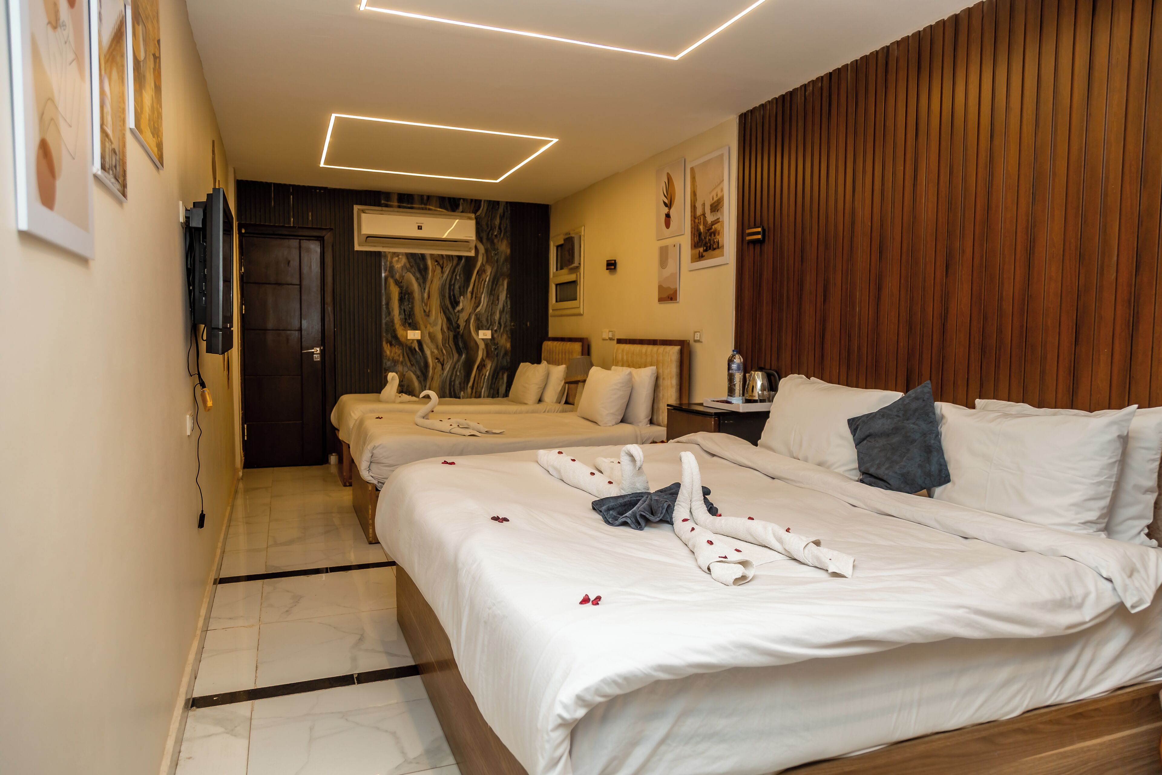 A hotel room with two beds, a wooden panel wall, a marble floor, and a modern light fixture.