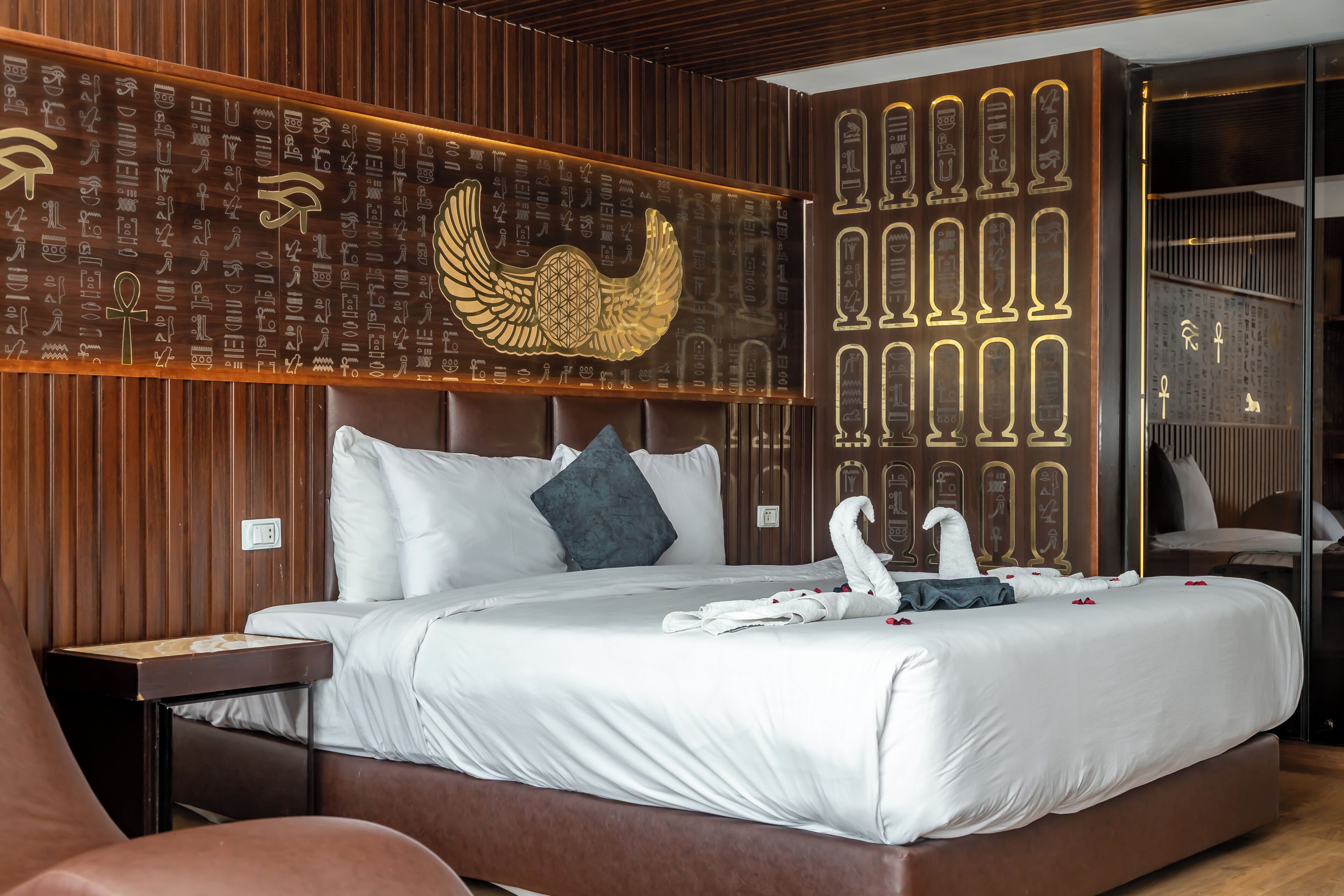 A hotel room with a large bed, wooden paneling, and wall decorations including Egyptian hieroglyphs and a golden winged figure.