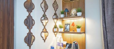 Un mostrador de recepción de hotel con espejos decorativos en la pared, un estante de madera con plantas, una lámpara y un hervidor.