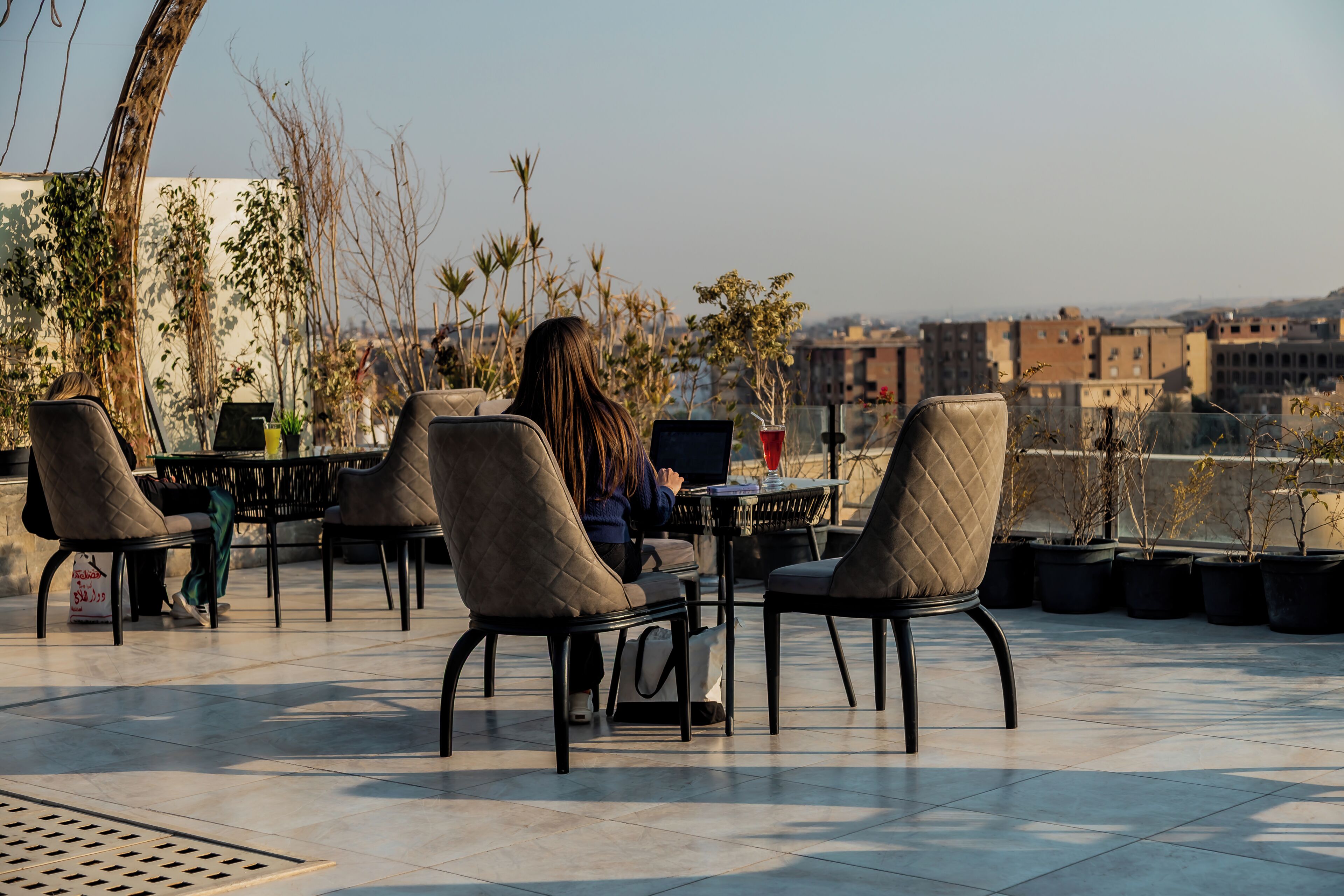 An outdoor seating area with chairs and tables, a laptop on one table, and a view of buildings in the background.