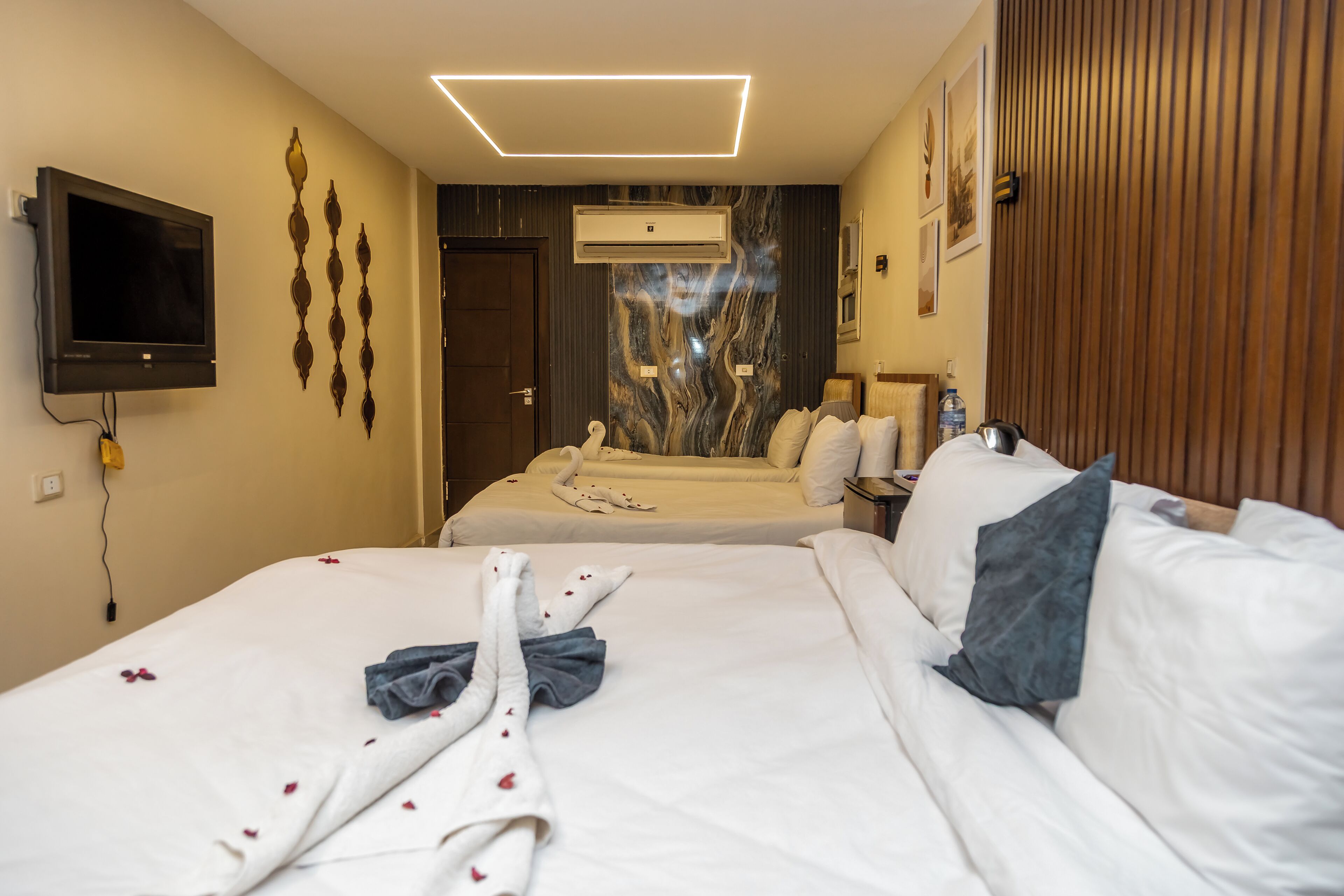 Habitación de hotel con dos camas, televisor, aire acondicionado y pared de paneles de madera.