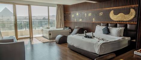A modern hotel room with a large bed, a desk, a chair, and a dining table with fruit.