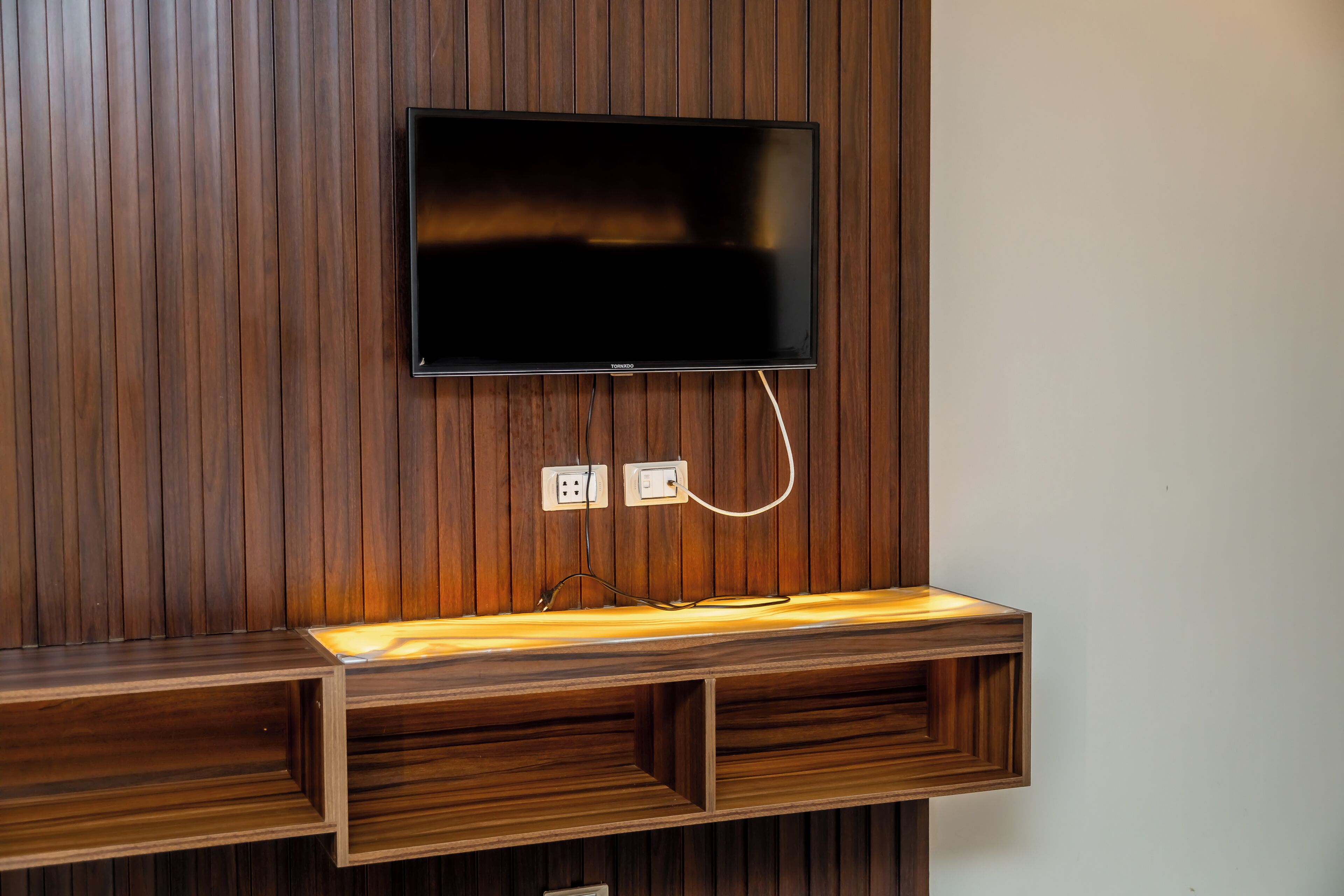 Een flatscreen televisie bevestigd aan een houten muur met ingebouwde planken eronder.