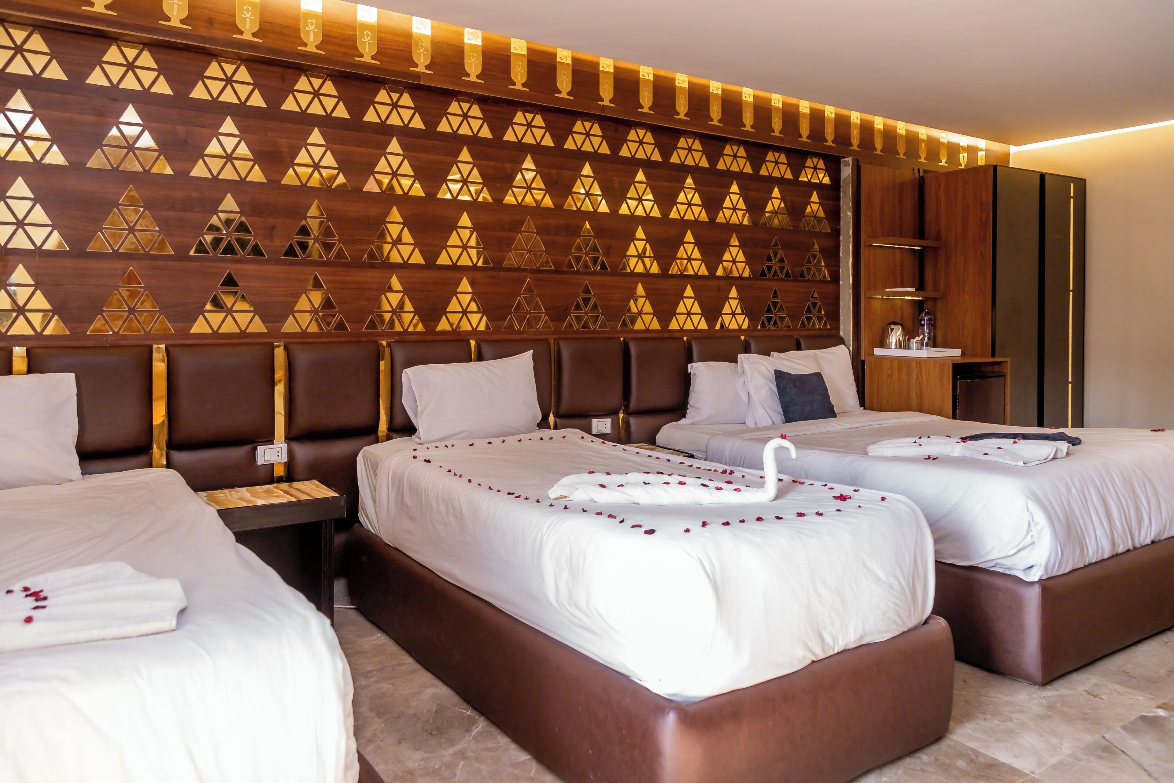 A hotel room with two beds, a wooden wall with geometric patterns, a bedside table, and a nightstand.