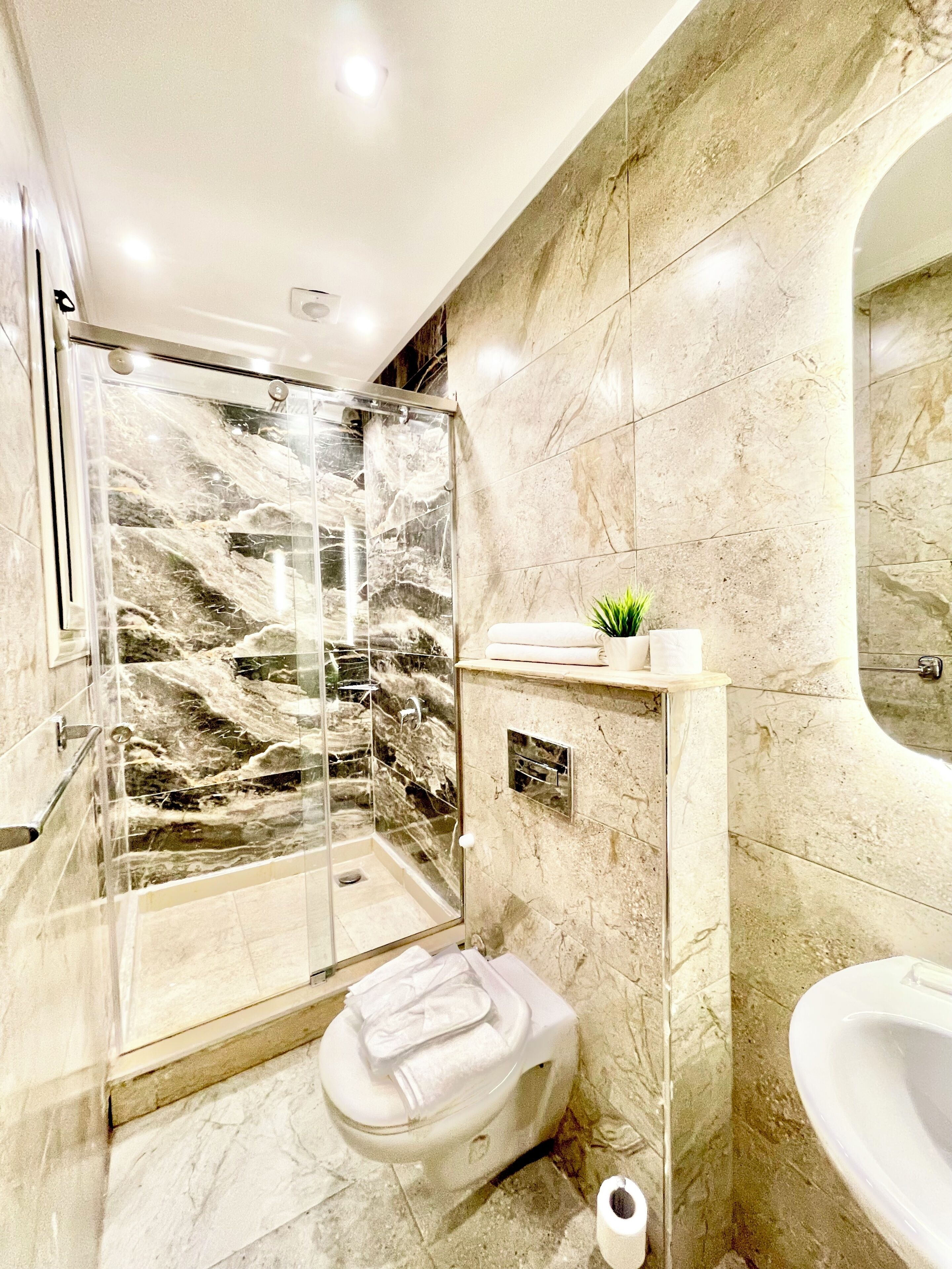 A modern bathroom with a glass-enclosed shower, a toilet, a sink, and a marble-tiled wall.