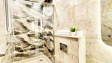A modern bathroom with a glass-enclosed shower, a toilet, a sink, and a marble-tiled wall.