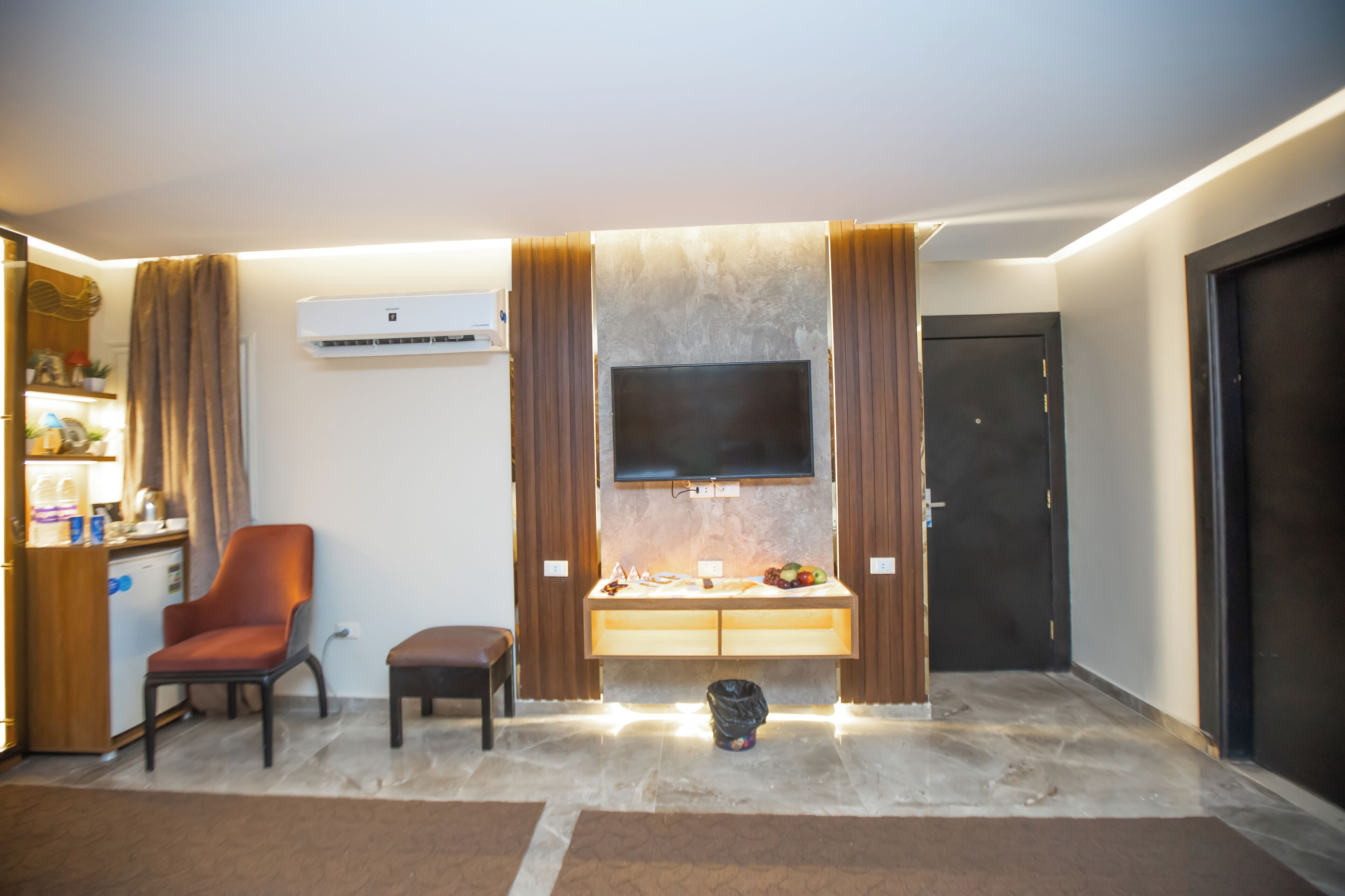 A modern living room with a flat-screen TV, a wooden cabinet, a chair, and a door.