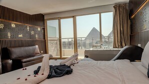 A hotel room with a bed, a sofa, a bathtub, and a large window with a view of a pyramid. - Hotel Comfort Giza (Giza)