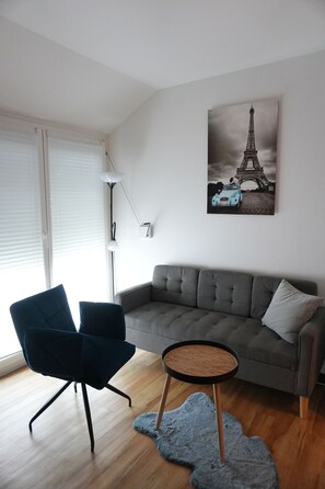 A modern living room with a grey sofa, a blue chair, a small round table, and a lamp.
