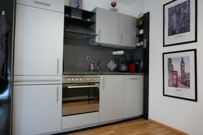 A kitchen with white cabinets, a stainless steel oven, and a microwave. There are framed pictures on the wall.