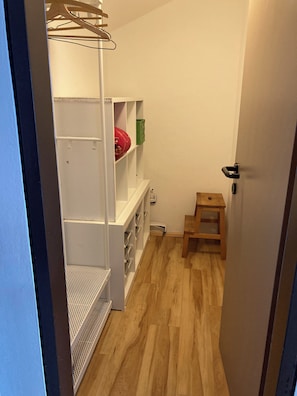 A narrow hallway with a wooden floor, a white shelving unit with storage, and a small wooden stool.
