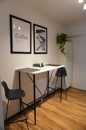 A small, modern kitchenette with a white countertop, two black chairs, and a white cabinet.