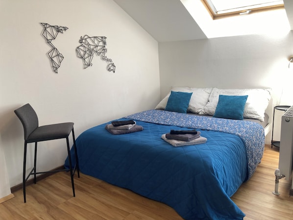 A bedroom with a bed, a chair, a radiator, and a skylight.