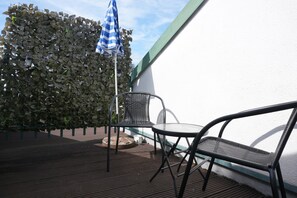 An outdoor seating area with two chairs and a table, a blue and white striped umbrella, and a hedge in the background.