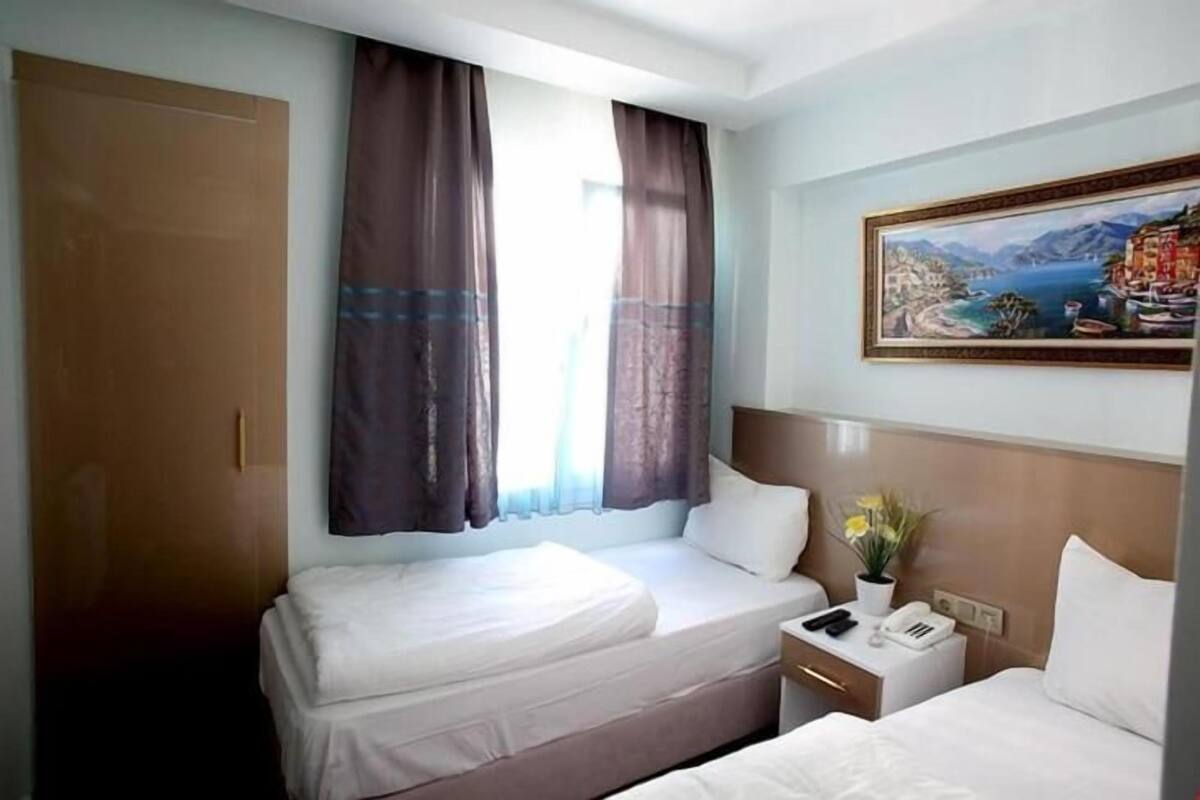 A hotel room with two beds, a nightstand, a painting, and a window with curtains.
