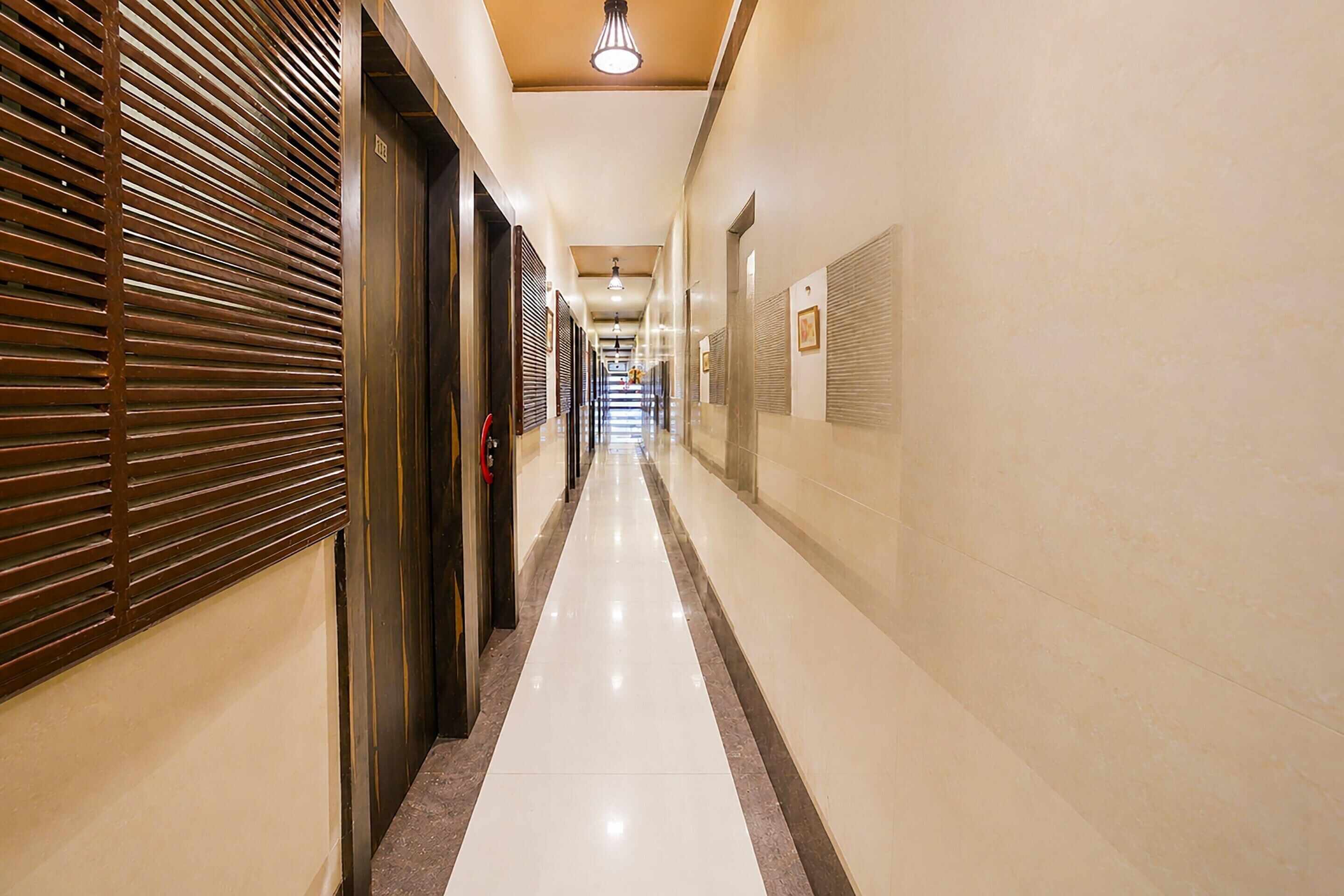 Un pasillo de hotel con piso pulido, puertas a la izquierda y una pared con cuadros enmarcados a la derecha.