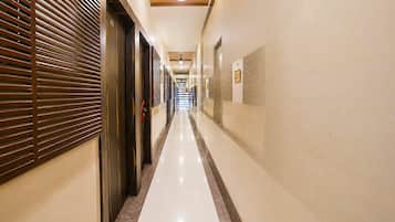 Un pasillo de hotel con piso pulido, puertas a la izquierda y una pared con cuadros enmarcados a la derecha.