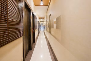 A hotel corridor with a polished floor, doors on the left, and a wall with framed pictures on the right.