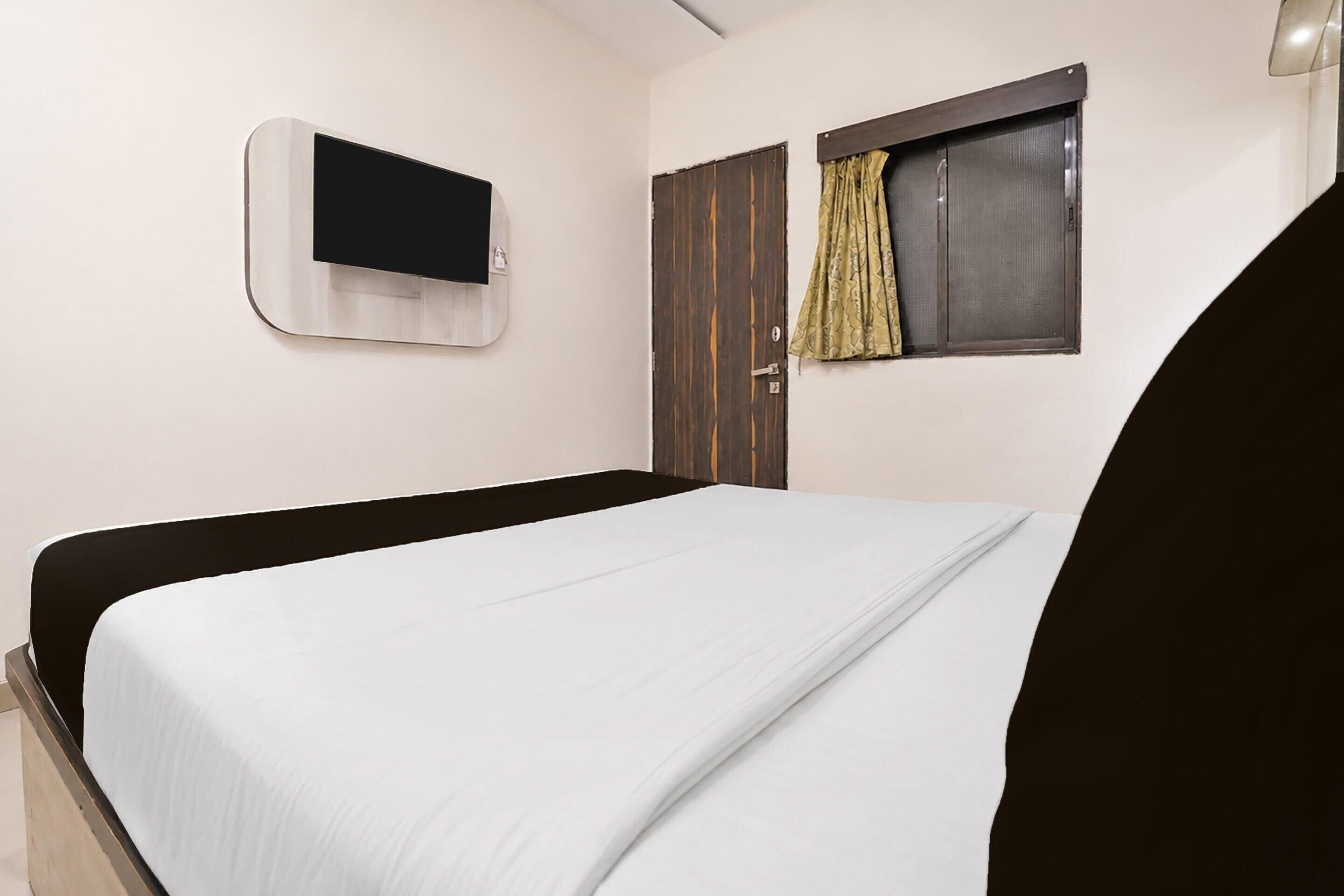 Una habitación con cama, televisor montado en la pared, una puerta y una ventana con cortinas.
