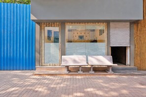 A modern building with a blue exterior wall, a wooden door, and a set of two stone benches in front.
