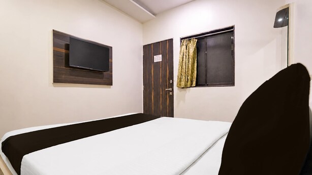 A single bed with a white mattress and a dark headboard in a room with white walls, a wooden door, and a window with curtains. - Classic Collection O Kurla BKC Mumbai (Mumbai)