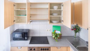 Una cocina con microondas, estufa y armarios abiertos.