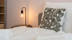 Una cama bien hecha con edredón blanco y almohada estampada con hojas.