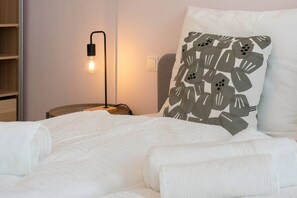 Ein ordentlich bezogenes Bett mit einer weißen Tagesdecke und einem Kopfkissen mit einem Blattmuster.