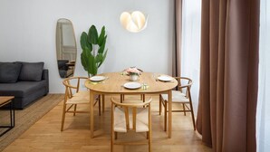 Uma sala de jantar com uma mesa de madeira redonda, seis cadeiras, um vaso de planta e um lustre.