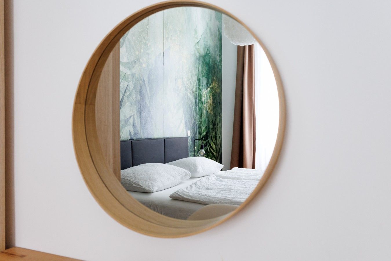 Une chambre à coucher avec un grand miroir rond qui reflète un lit, une tête de lit et un mur orné d’un motif texturé.