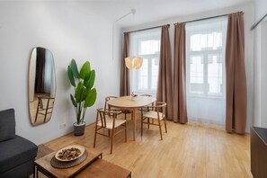 A modern living room with a round wooden table, two chairs, a potted plant, a mirror, and a sofa. - Oona Residence Vienna (Österreich)