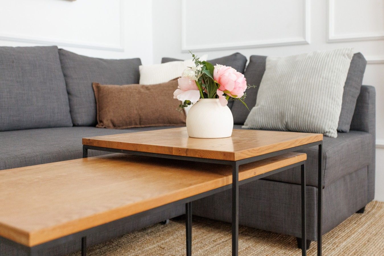 Un salon moderne avec un canapé gris, une table basse en bois et un vase blanc orné de fleurs.