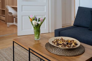 Ein Holztisch mit einer gewebten Tischmatte, einer Glasvase mit Blumen und einer Schale voller Nüsse.