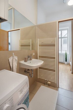 A modern bathroom with a sink, mirror, towel rack, and a shower area with horizontal blinds. - Oona Residence Vienna (Österreich)
