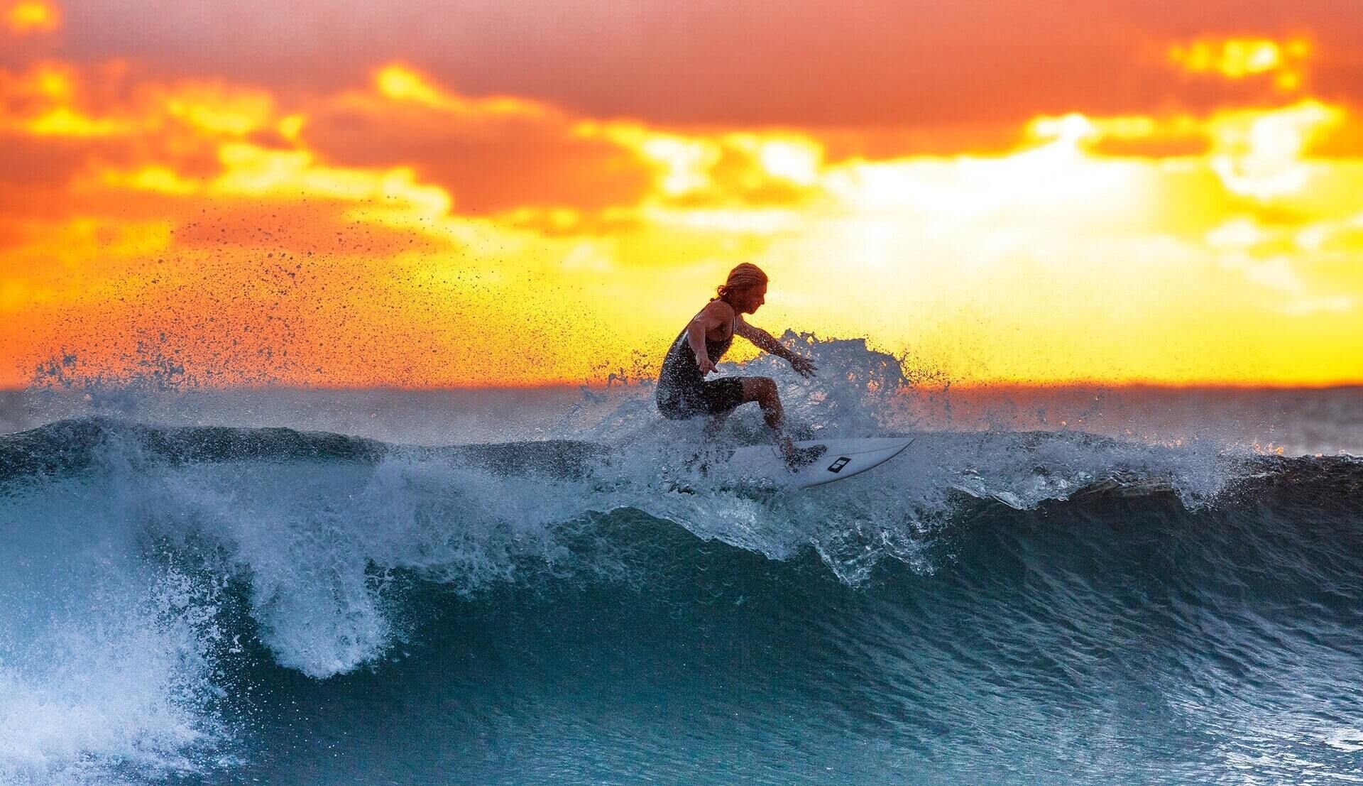 A person surfing on a wave with a sunset in the background.
